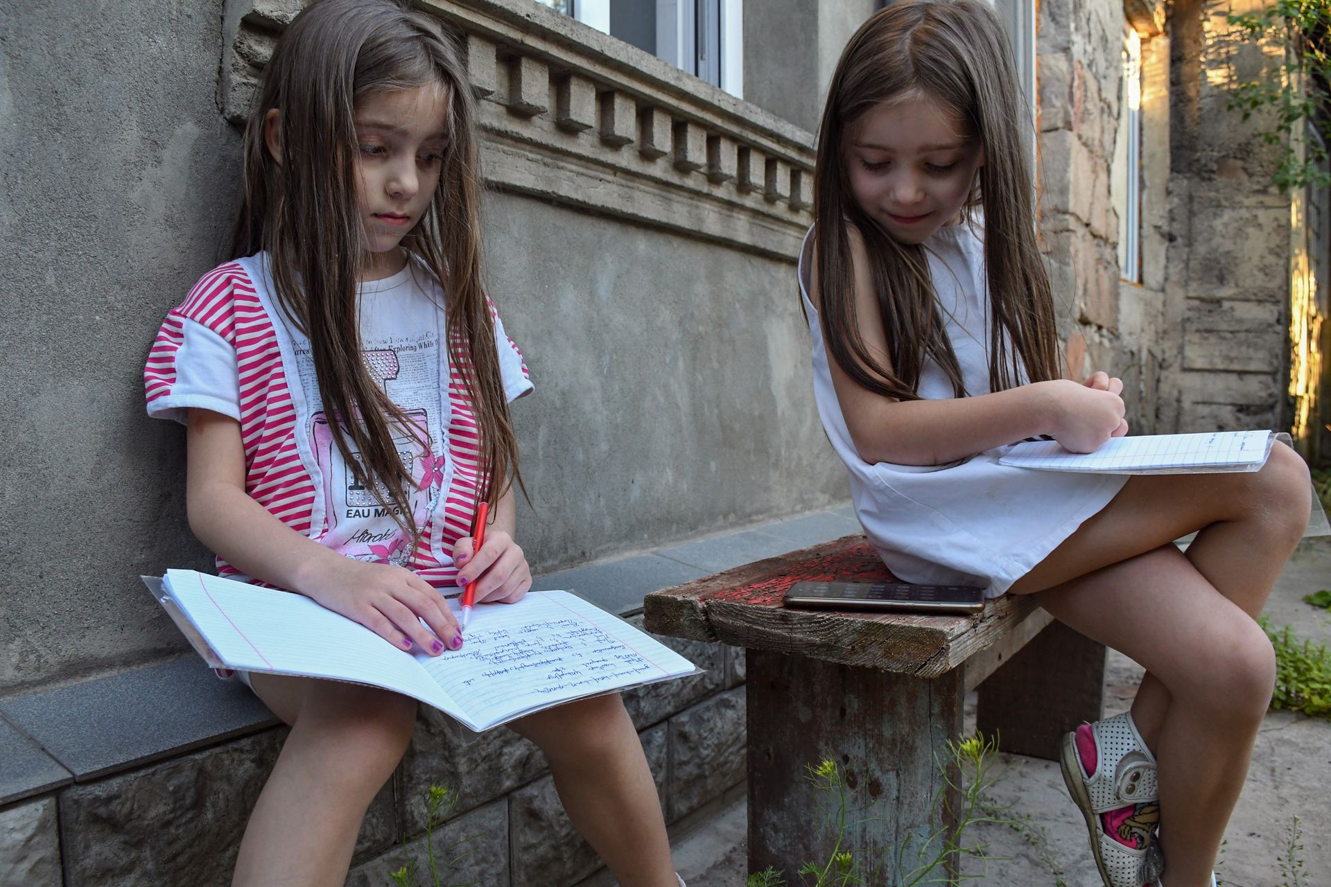 two girls sitting outside, reading a book