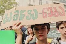 კლიმატის აქციაზე გოგონა დგას ბანერით, რომელსაც აწერია გამწვა-ნება